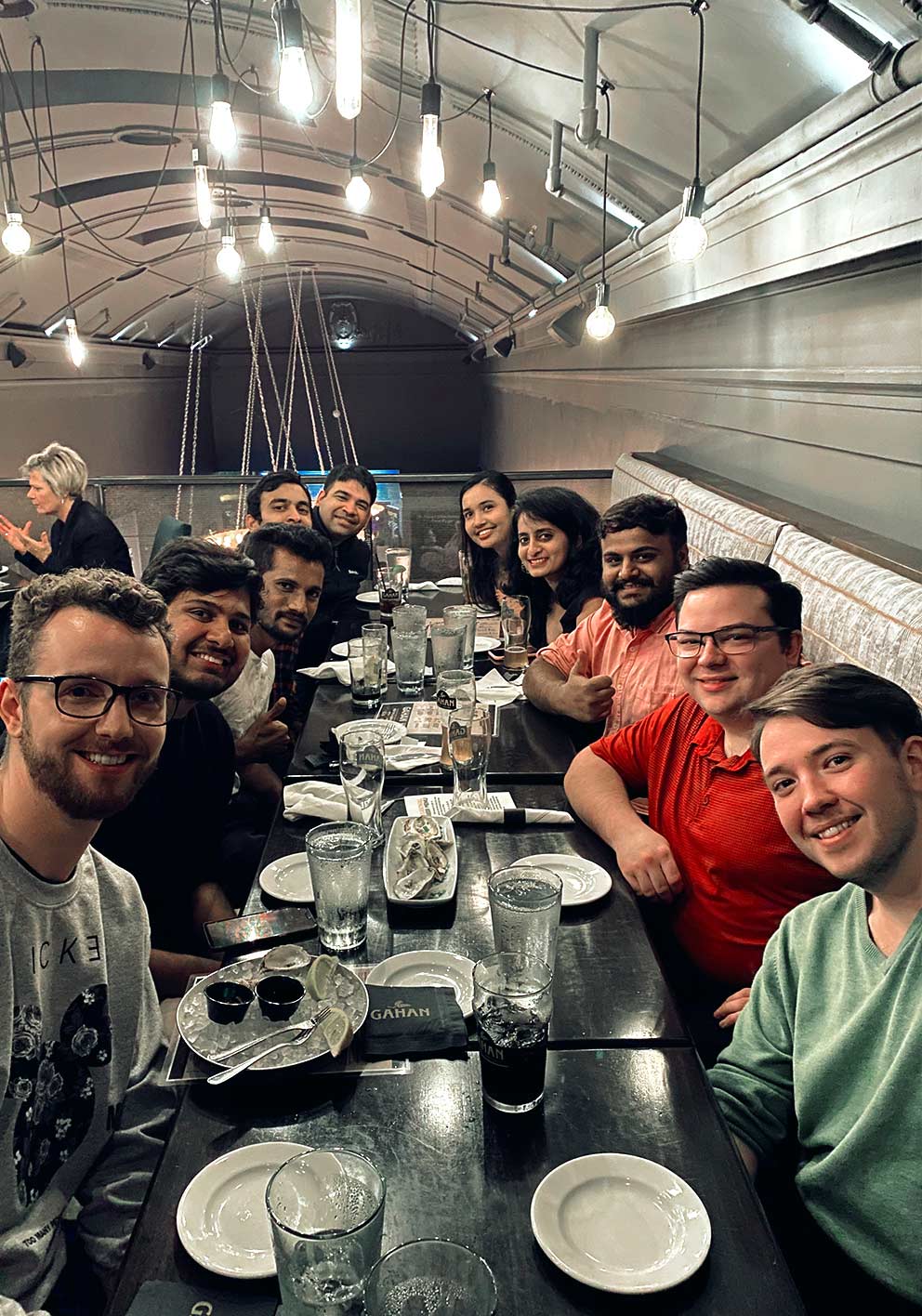 A group of Tarkans sitting down at a long black dinner table with empty plates in front of them, looking into the camera and smiling